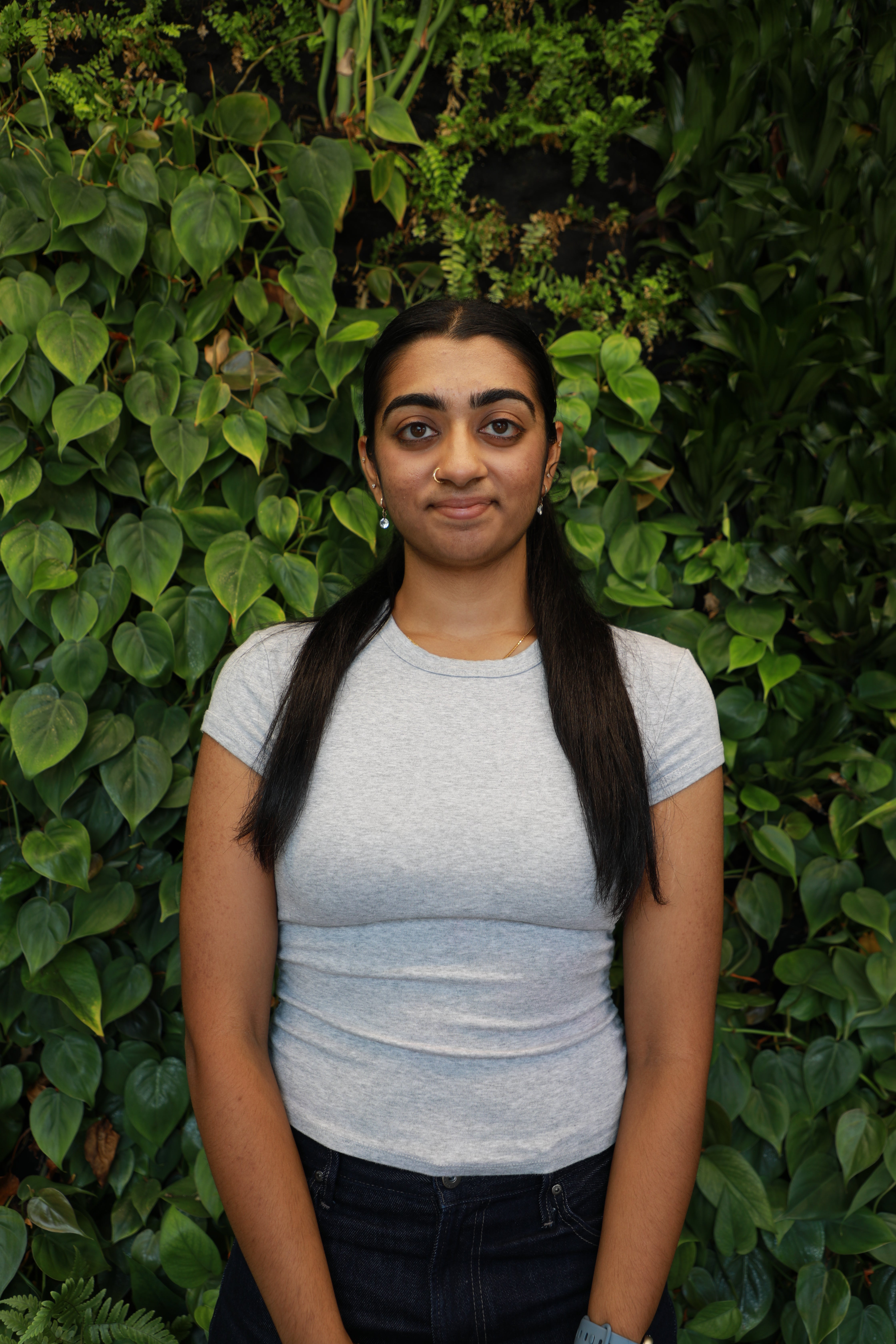 Harshitha Jeyakumar smiling in front of green wall.