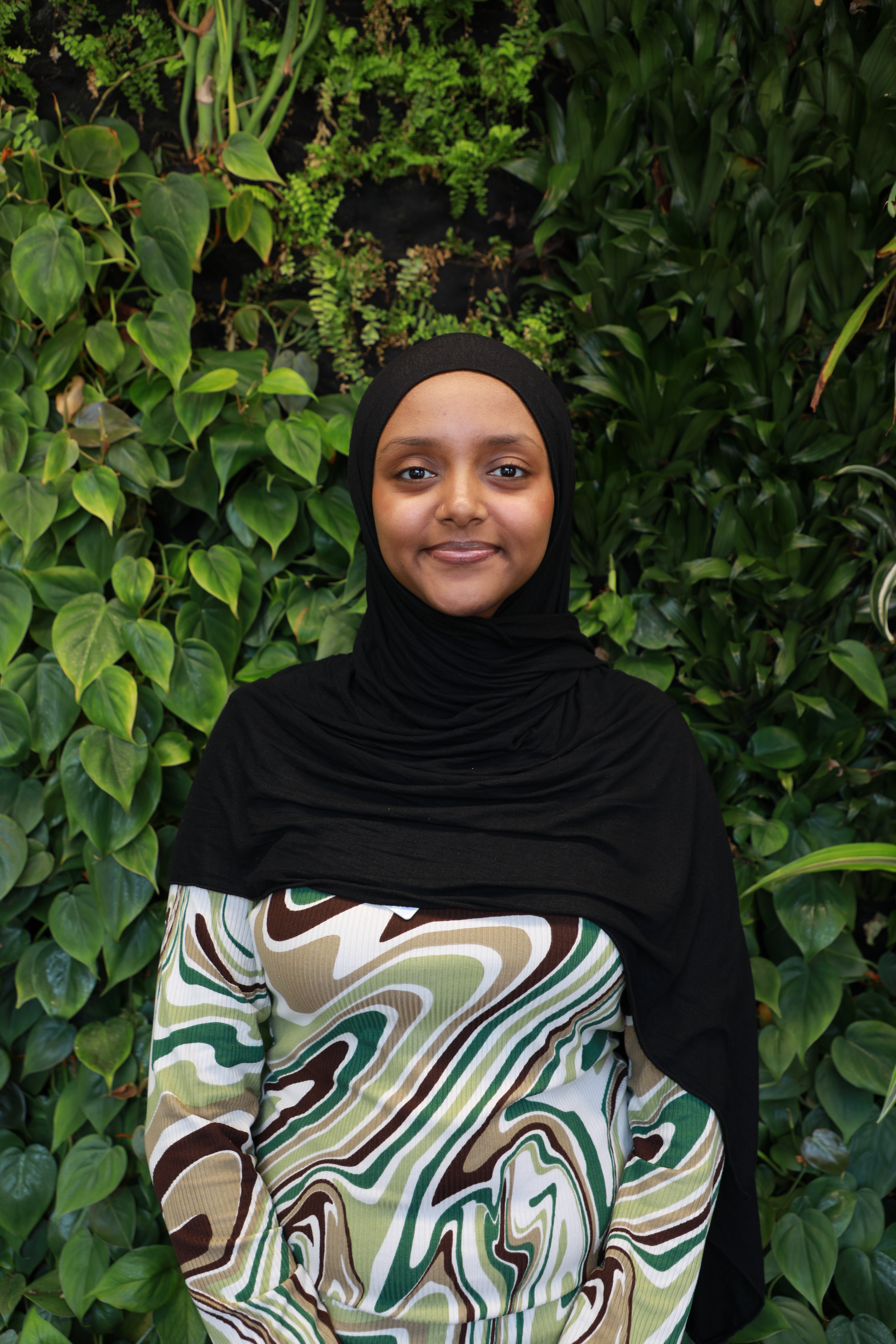 Tasneem smiling in front of green wall.