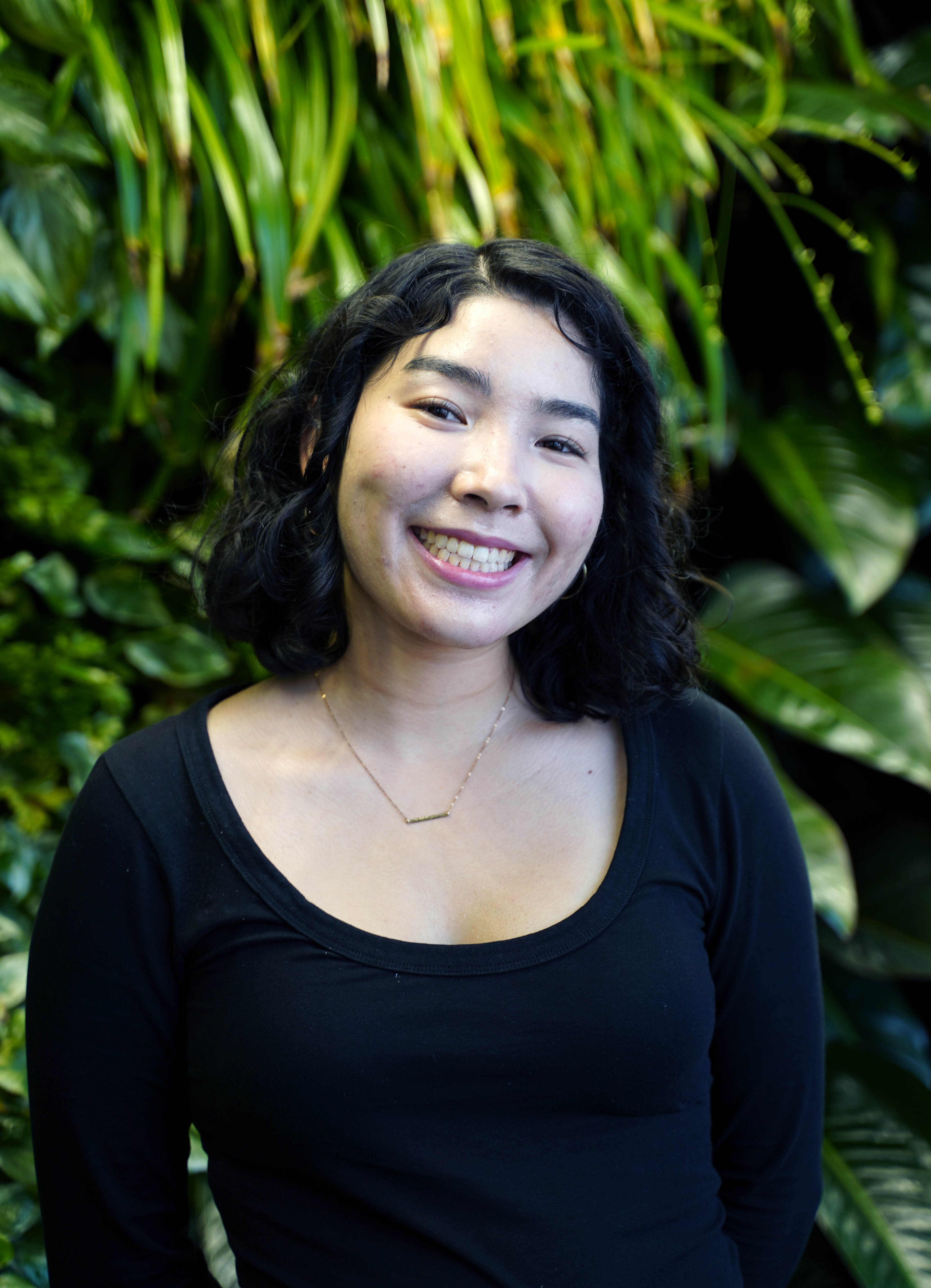 Ava Lamberty in a black shirt with a plant backdrop. 