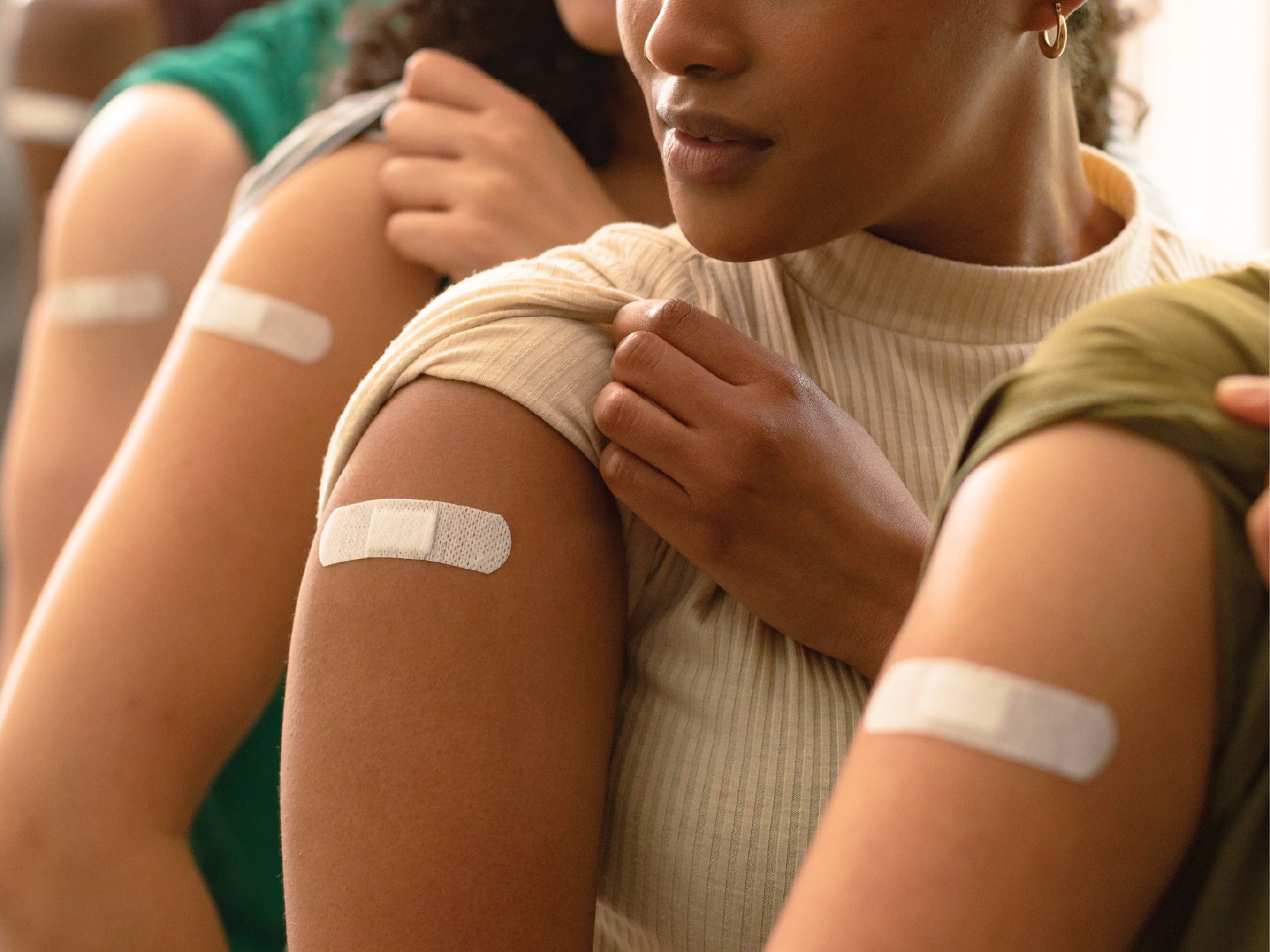 People hold up their sleeves, revealing band-aids covering the site of recent immunization injections.