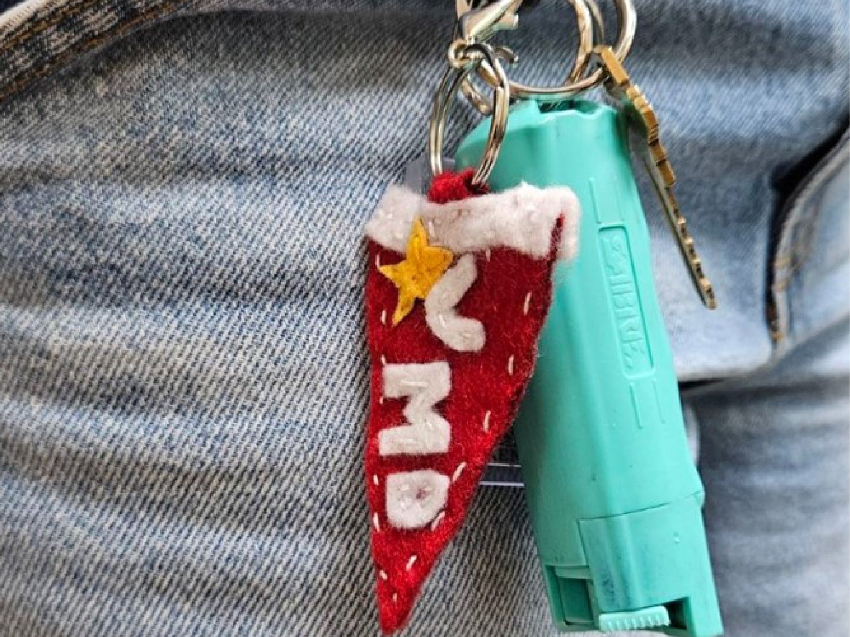 A handmake felt pennant keychain hangs from a person's belt loop.
