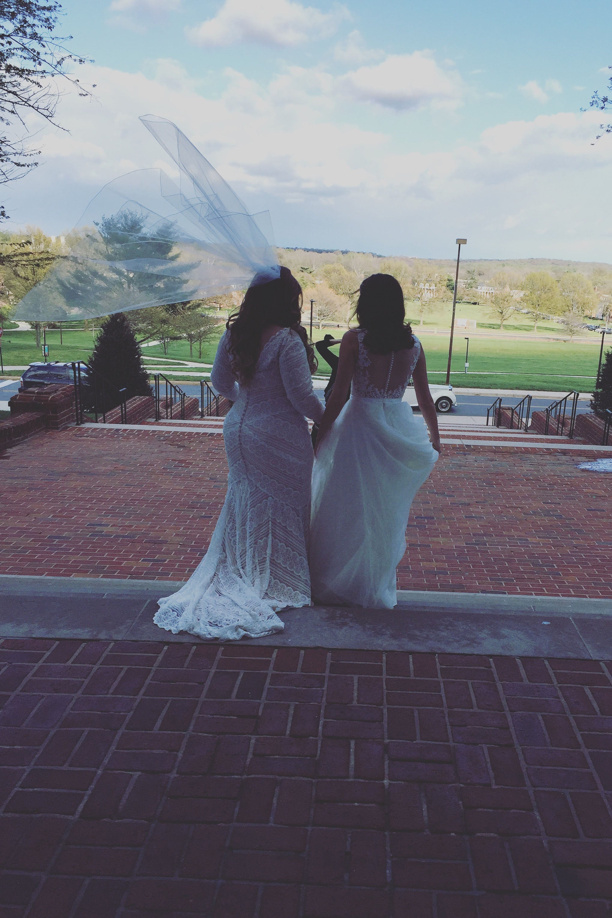 Two brides pose in front of Memorial Chapel in wedding gowns.