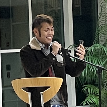 Tight framed photo of a figure smiling while singing into a microphone