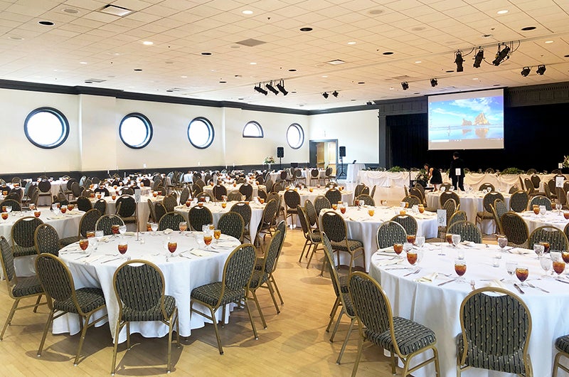 Tables adorned with tablecloths, cutlery and served drinks for an event in the Colony Ballroom at Stamp.