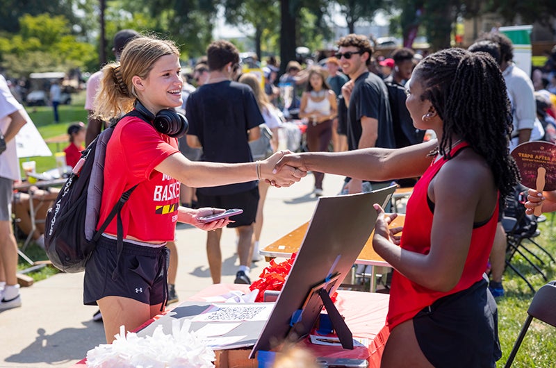 two students shake hands over a booth table during First Look Fair on McKeldin Mall.
