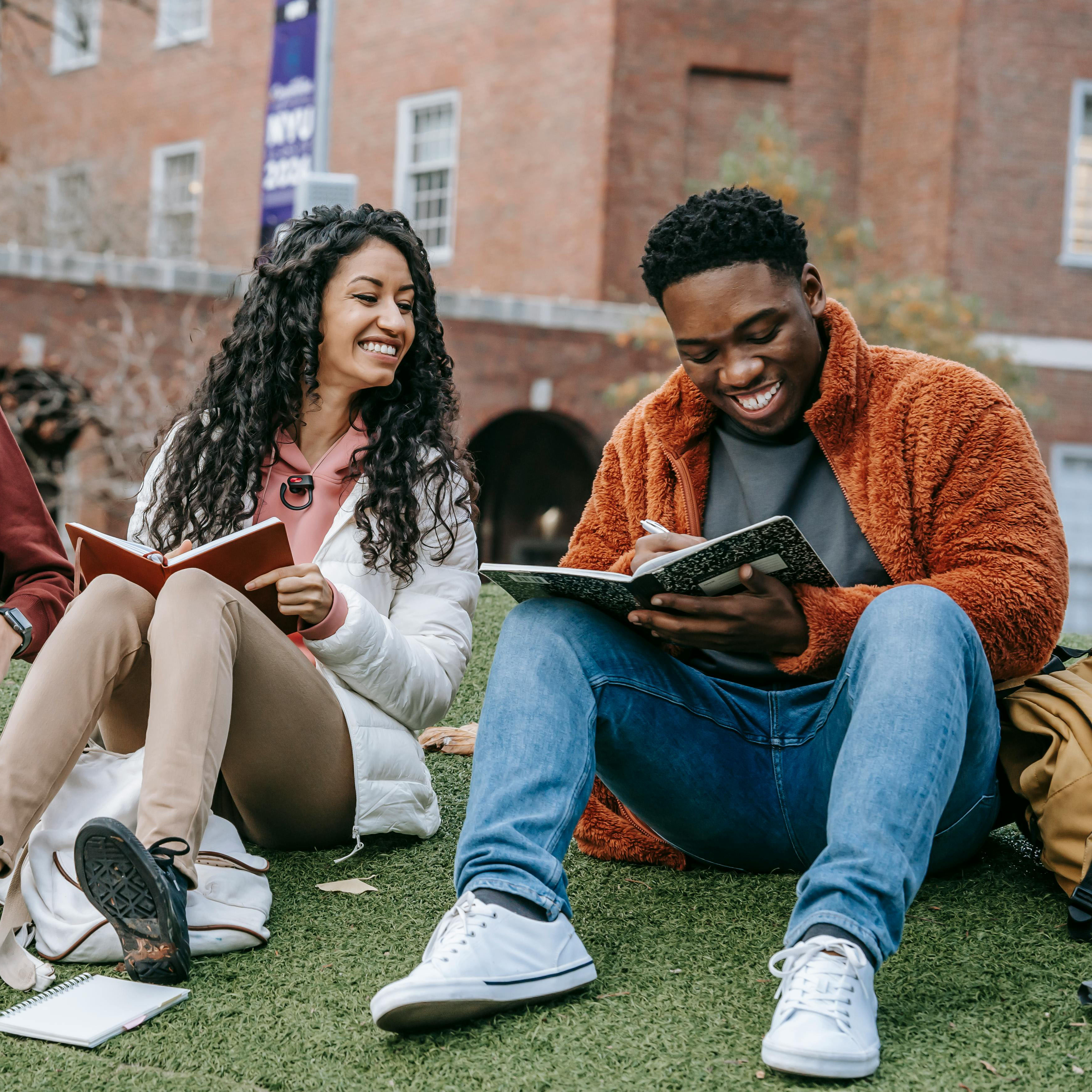 two students sitting outside writing on a notebook
