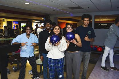 group of five students, one holding a bowling ball, at the TerpZone bowling lane.