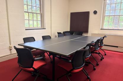 A meeting room in the Chapel featuring a large conference table surrounded by black rolling chairs with vibrant red carpet.