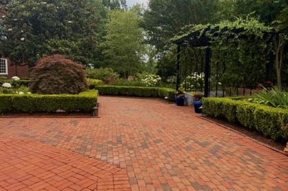 A red brick pathway in a garden courtyard with a metal pergola covered in climbing green vines and neatly manicured hedges.