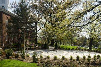 An outdoor circular stone walking labyrinth surrounded by a ring of small green hedges.