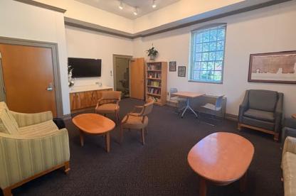 indoor lounge area in the Chapel featuring armchairs, oval wooden coffee tables, a wall-mounted TV and a large window.