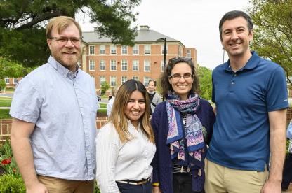Four smiling campus chaplains posing together outdoors with a brick university building in the background.