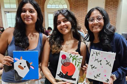 Three students holding paintings created at Studio A's Paint Night