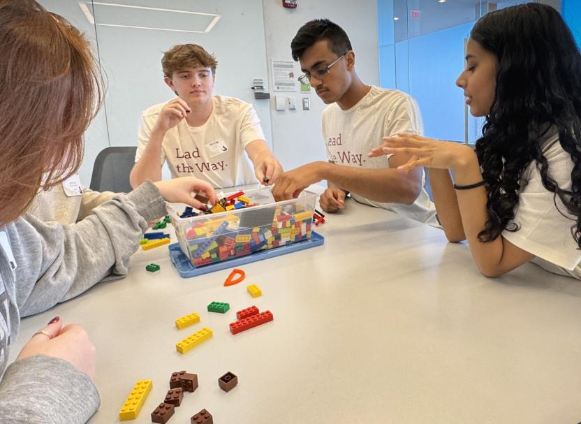 four students around a table with a bin of legos in the middle