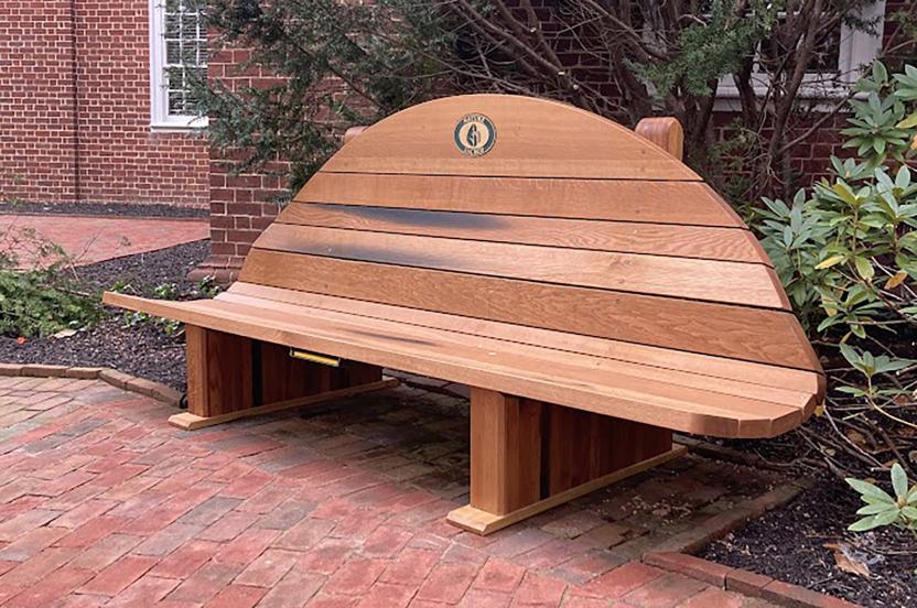 A polished wooden bench with a rounded, fan-shaped backrest outside Memorial Chapel.
