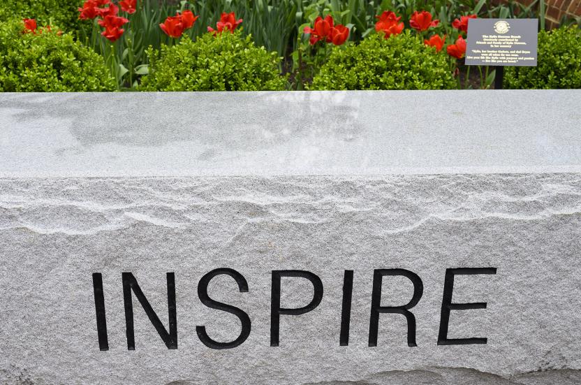 A close-up of a stone garden bench engraved with the word "INSPIRE" in all capital letters.