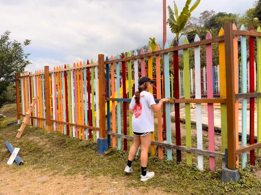 An AB team member paints a fence 