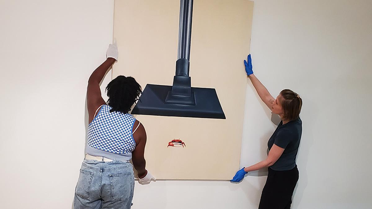 Two people installing a painting on the Stamp Gallery's Wall
