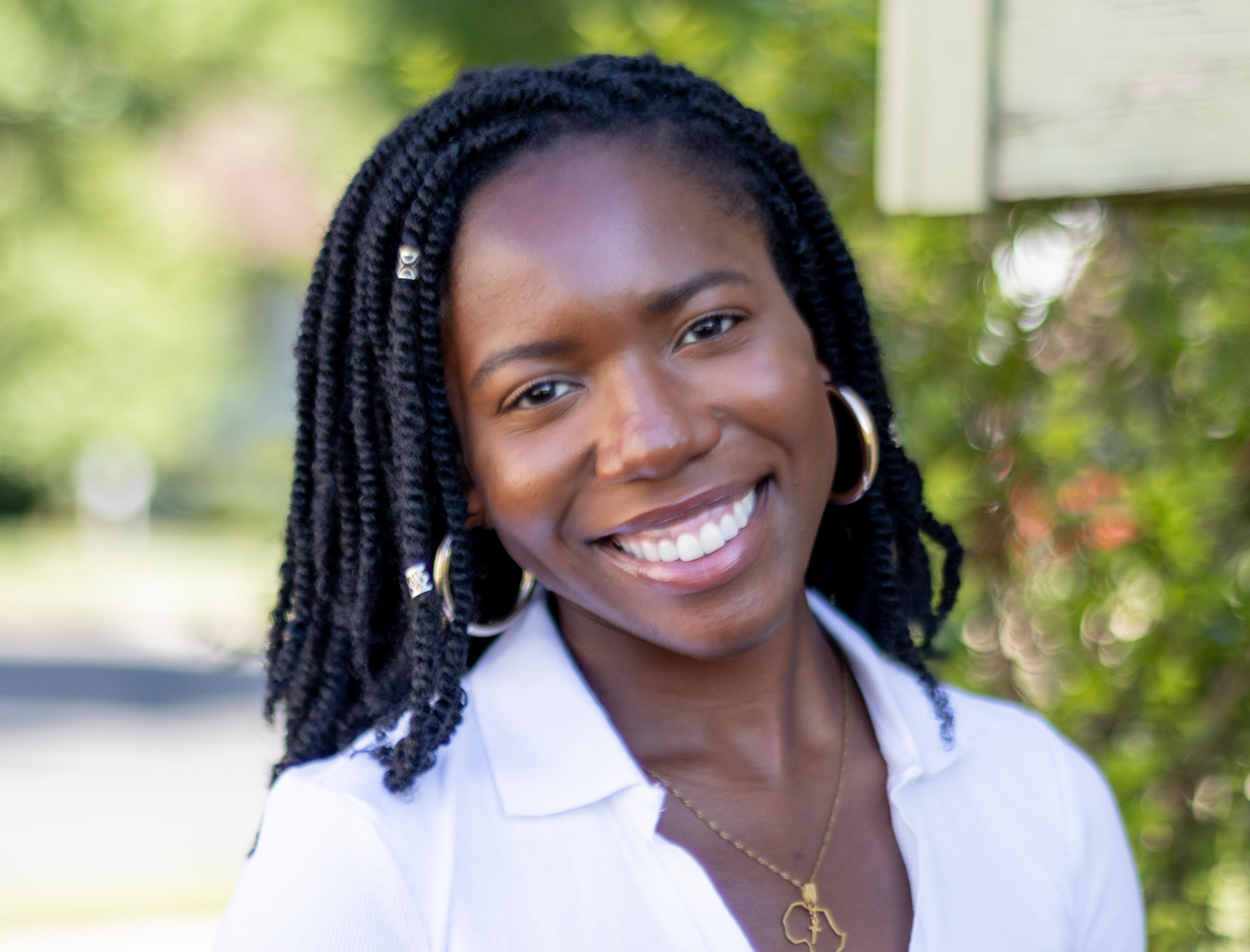 Picture of Oyin smiling in front of a leafy green background