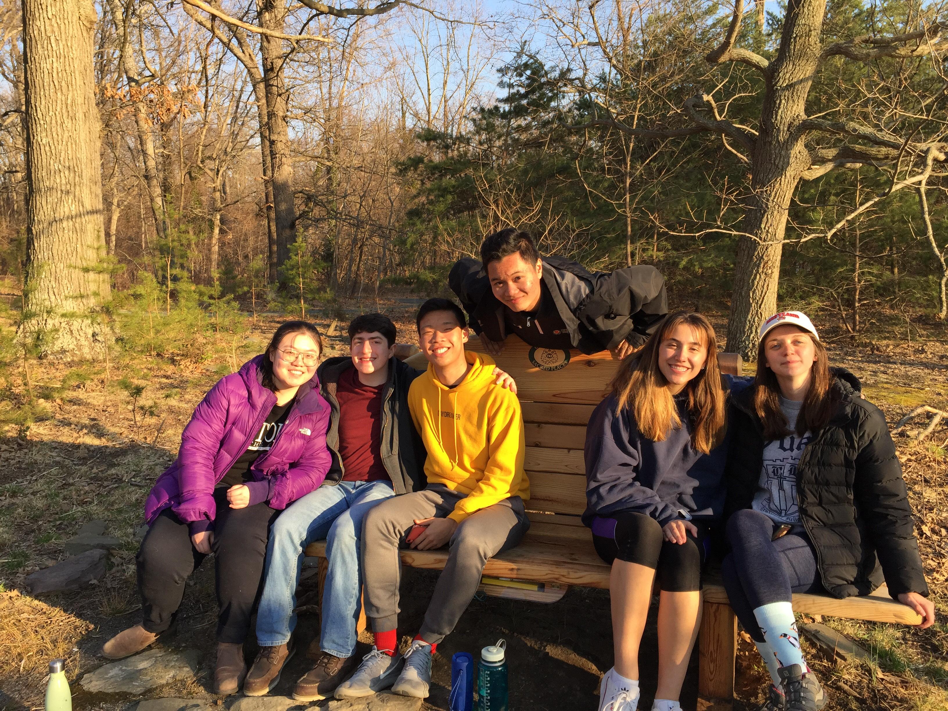 A photo of 6 Alternative Breaks Volunteers sitting together on a bench after doing some service work