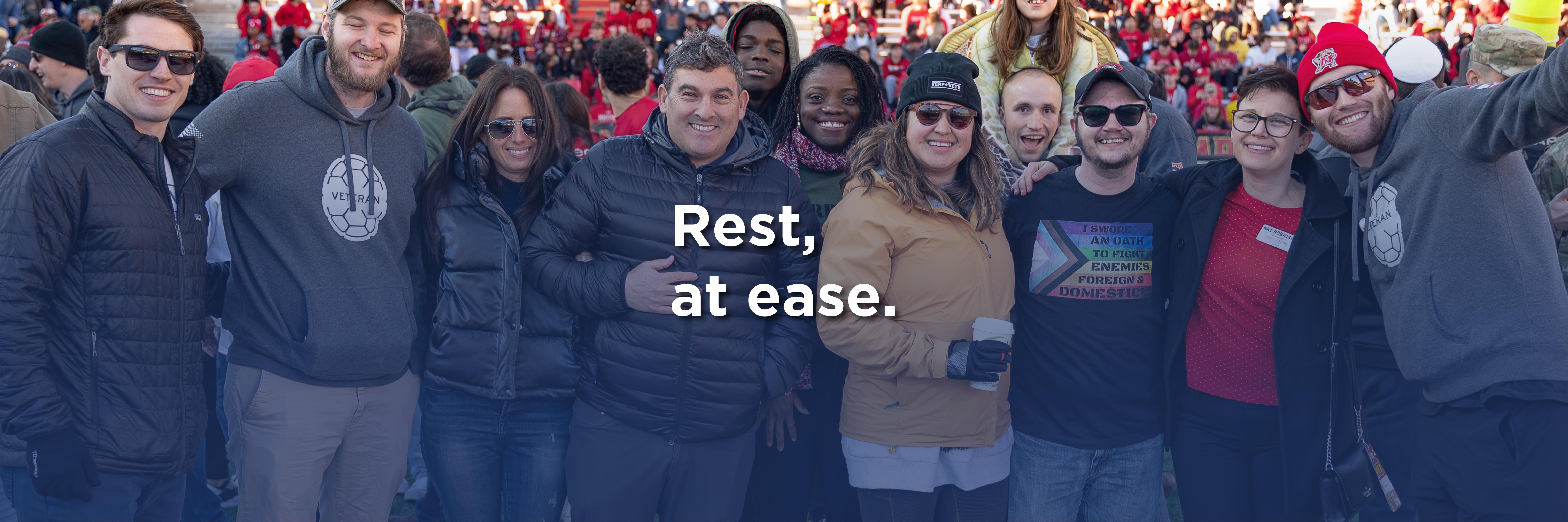 The text "Rest, at ease." superimposed on an image of a group of people at a football game