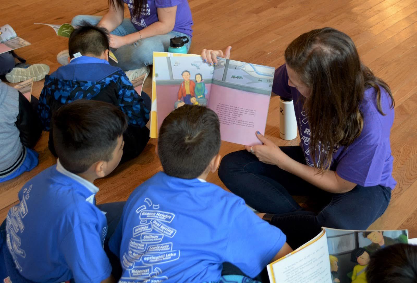 college student reading to younger students
