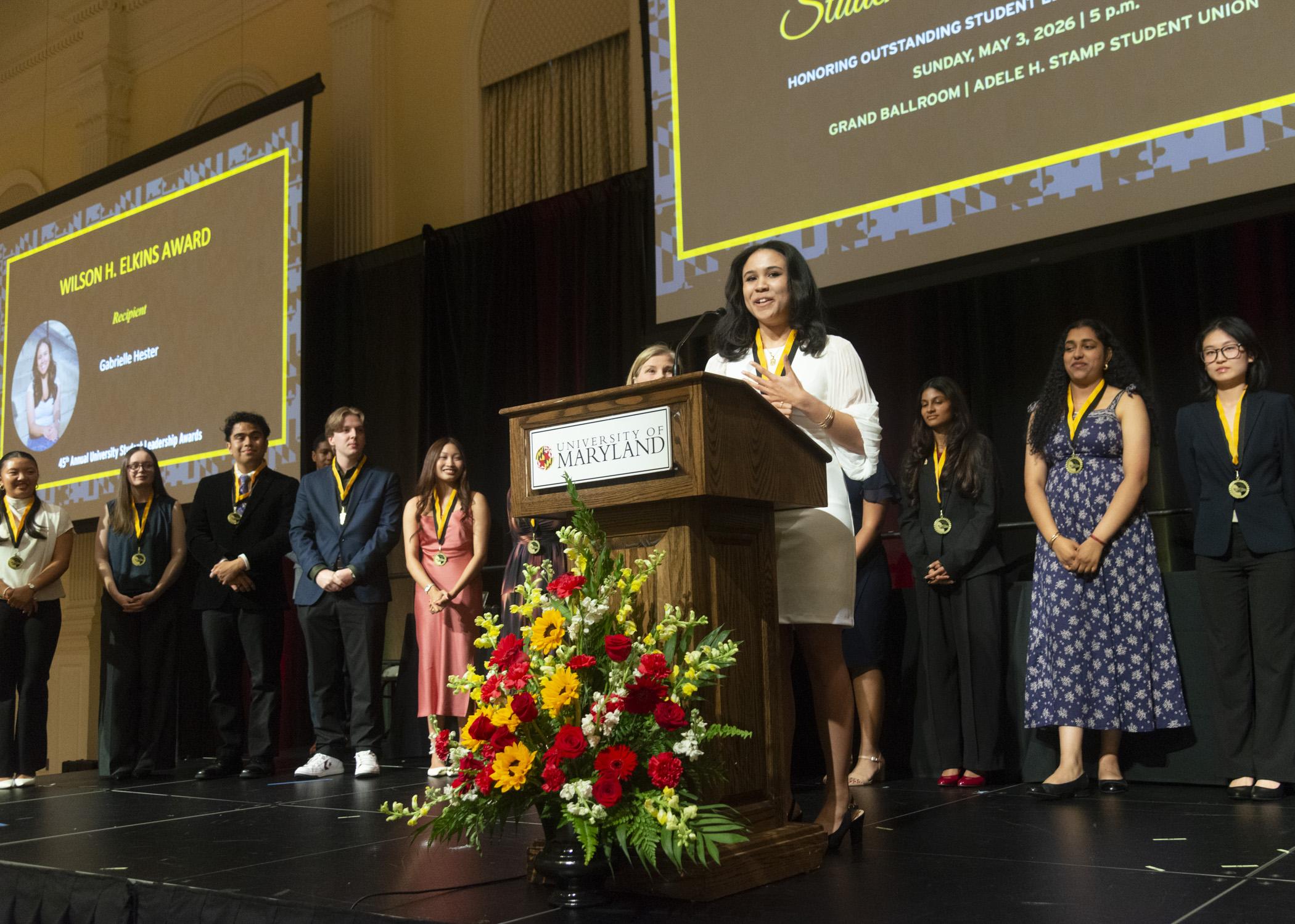 A photo of the Wilson H. Elkins Recipient giving a speech on stage with Maryland Medallion Society Members behind her