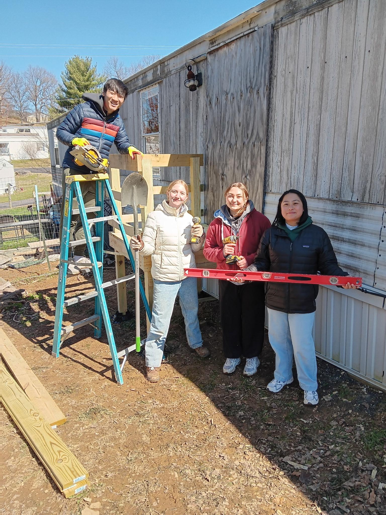 4 students in AB take a break from repairing a house to take a photo