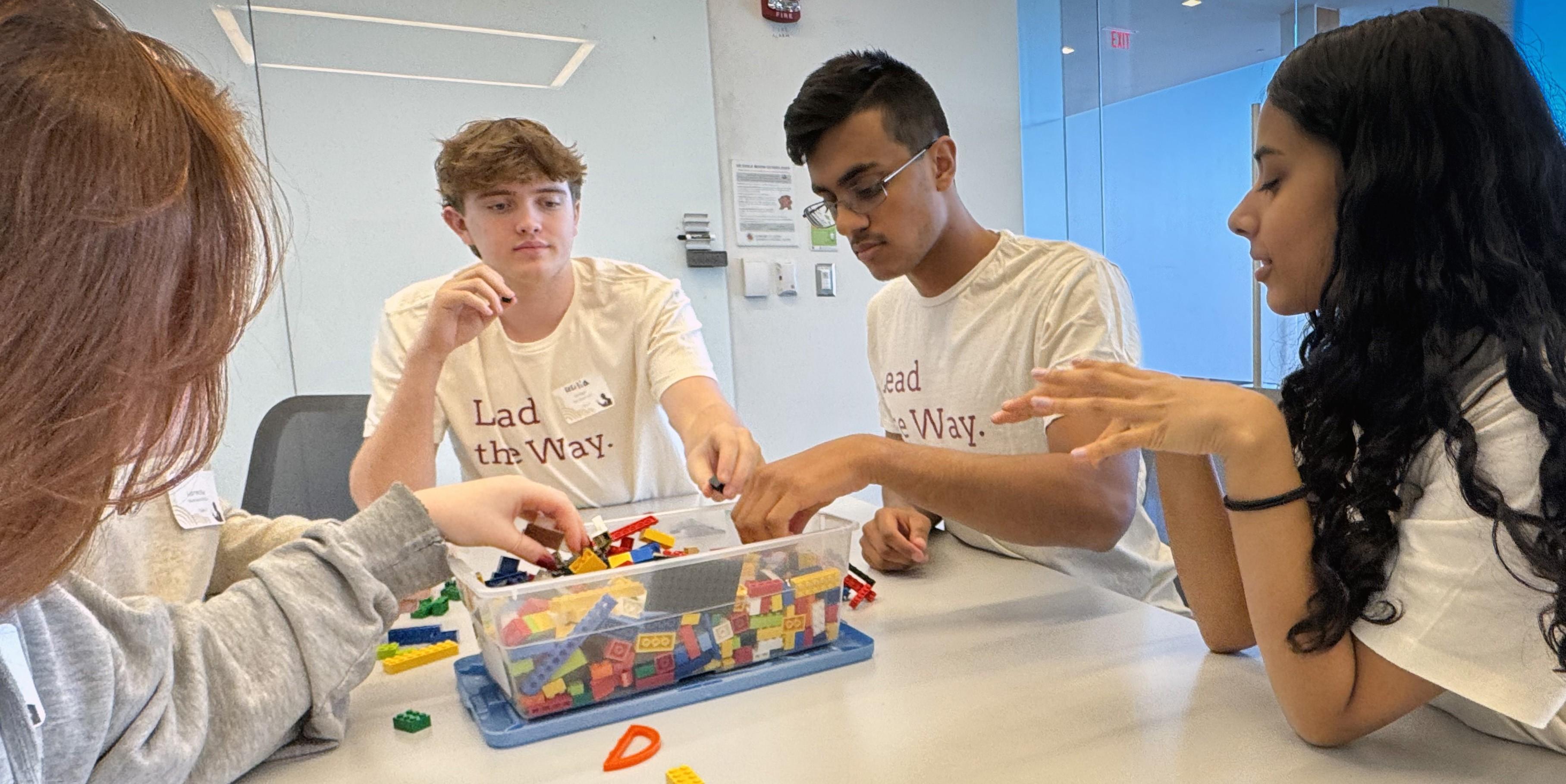 group of 4 students sitting around a table with a bin of legos in the center