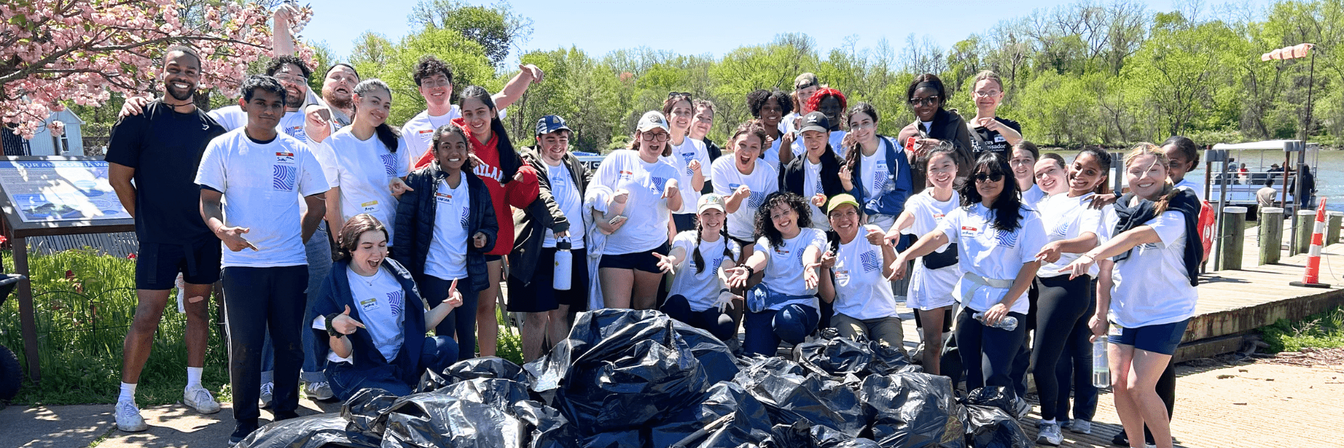 A large group of staff and students in matching white Restorative Practices shirts in front of a collection of trash bags