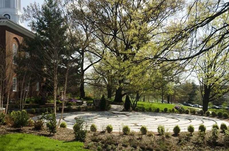 An outdoor circular stone walking labyrinth surrounded by a ring of small green hedges.