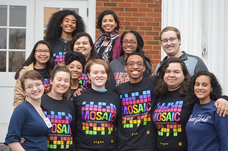 A diverse group of students wearing matching t-shirts smiling and posing together outside a building.
