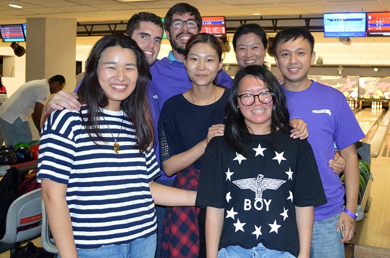 A group of seven smiling students posing together for a photo inside the Stamp bowling alley.