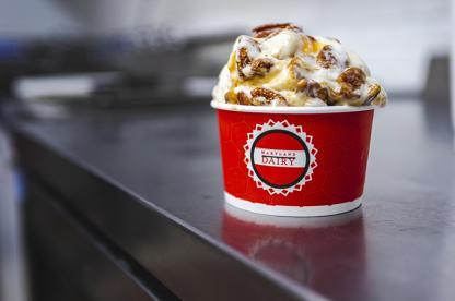Scoop of vanilla ice cream topped with caramel and nuts in a red cup.