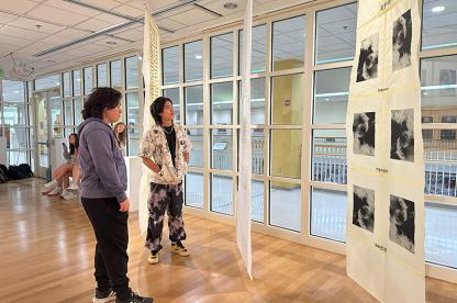 Two visitors look at a hanging fabric artwork installation inside the Stamp Gallery.