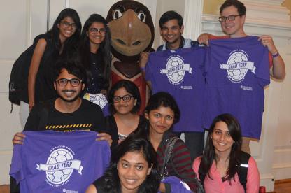 A group of graduate students posing together with the Testudo turtle mascot while holding up purple "Grad Terp" t-shirts.