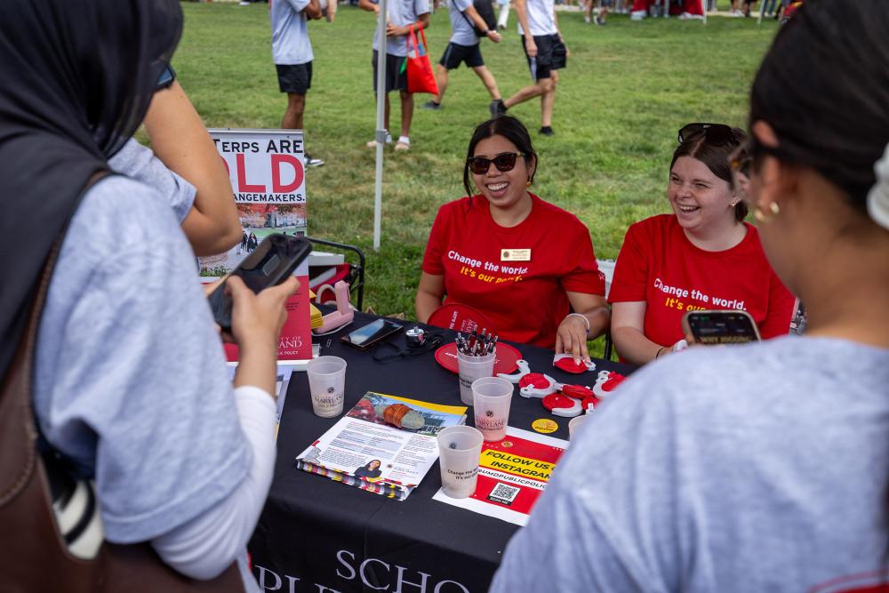 Two volunteers smile at an outdoor info table for during FreeFest on McKeldin Mall.